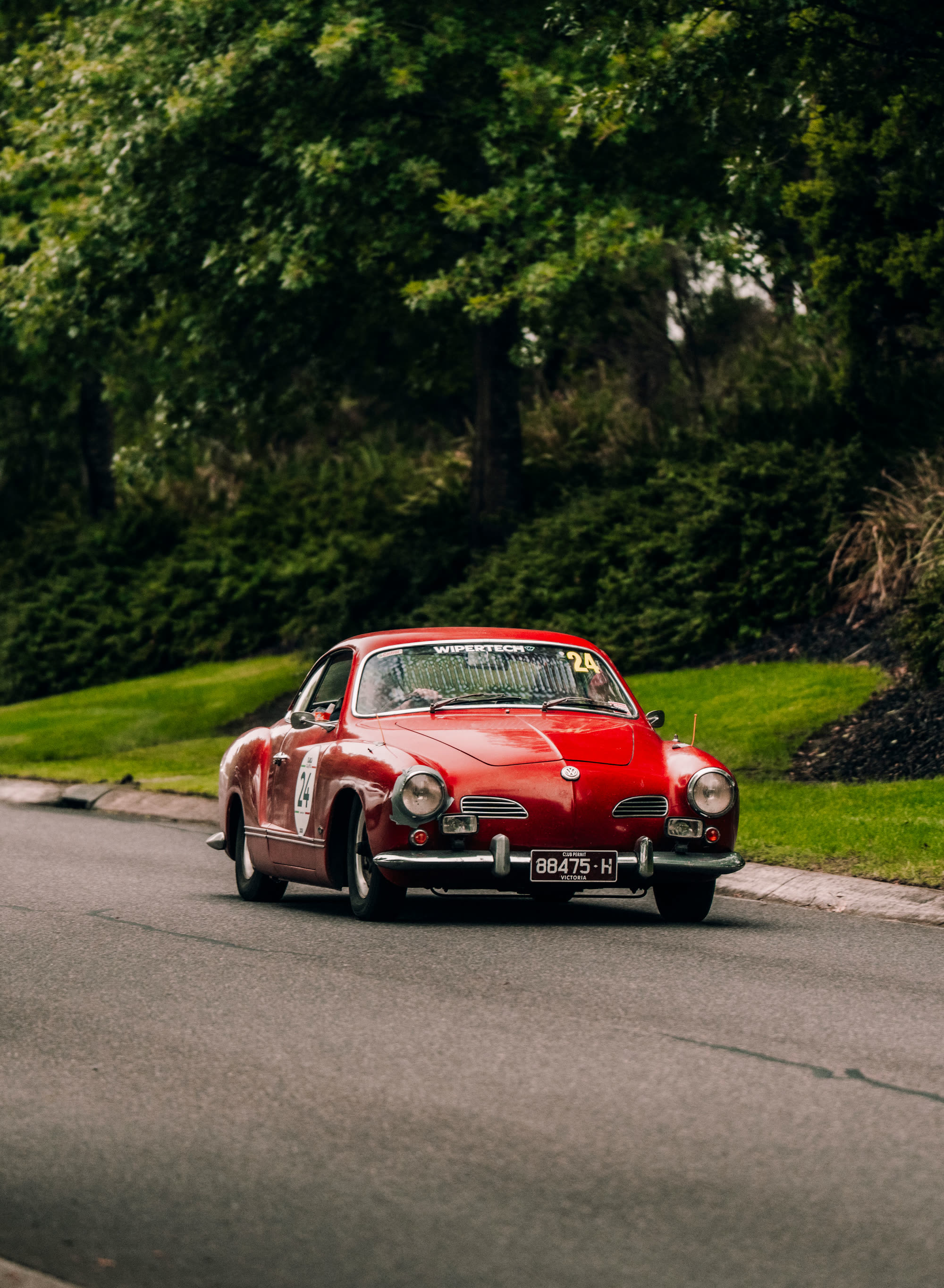 A red Karmann Ghia running number 24 on a tree-lined road