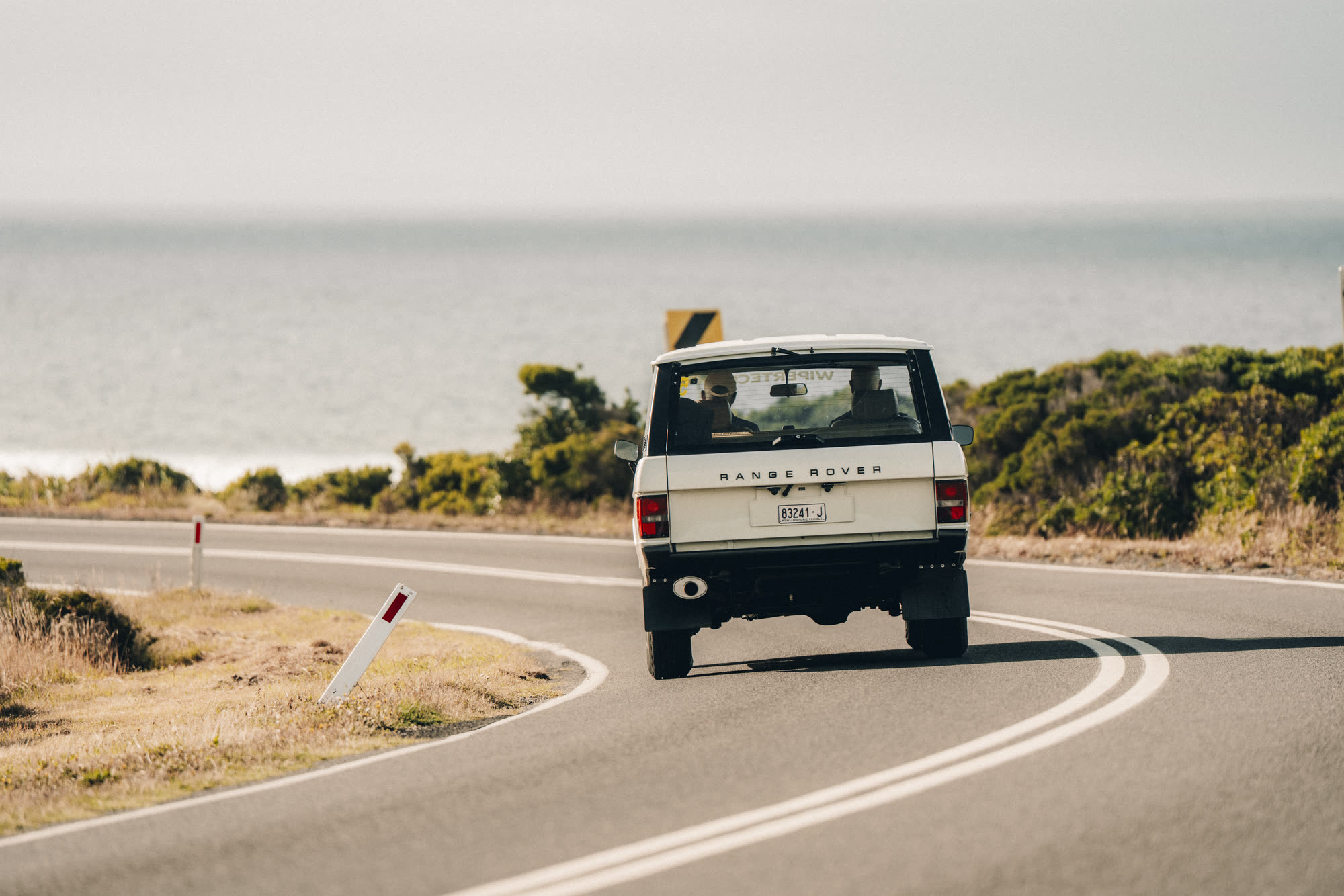 A cream Range Rover Classic on a coast road with the ocean behind