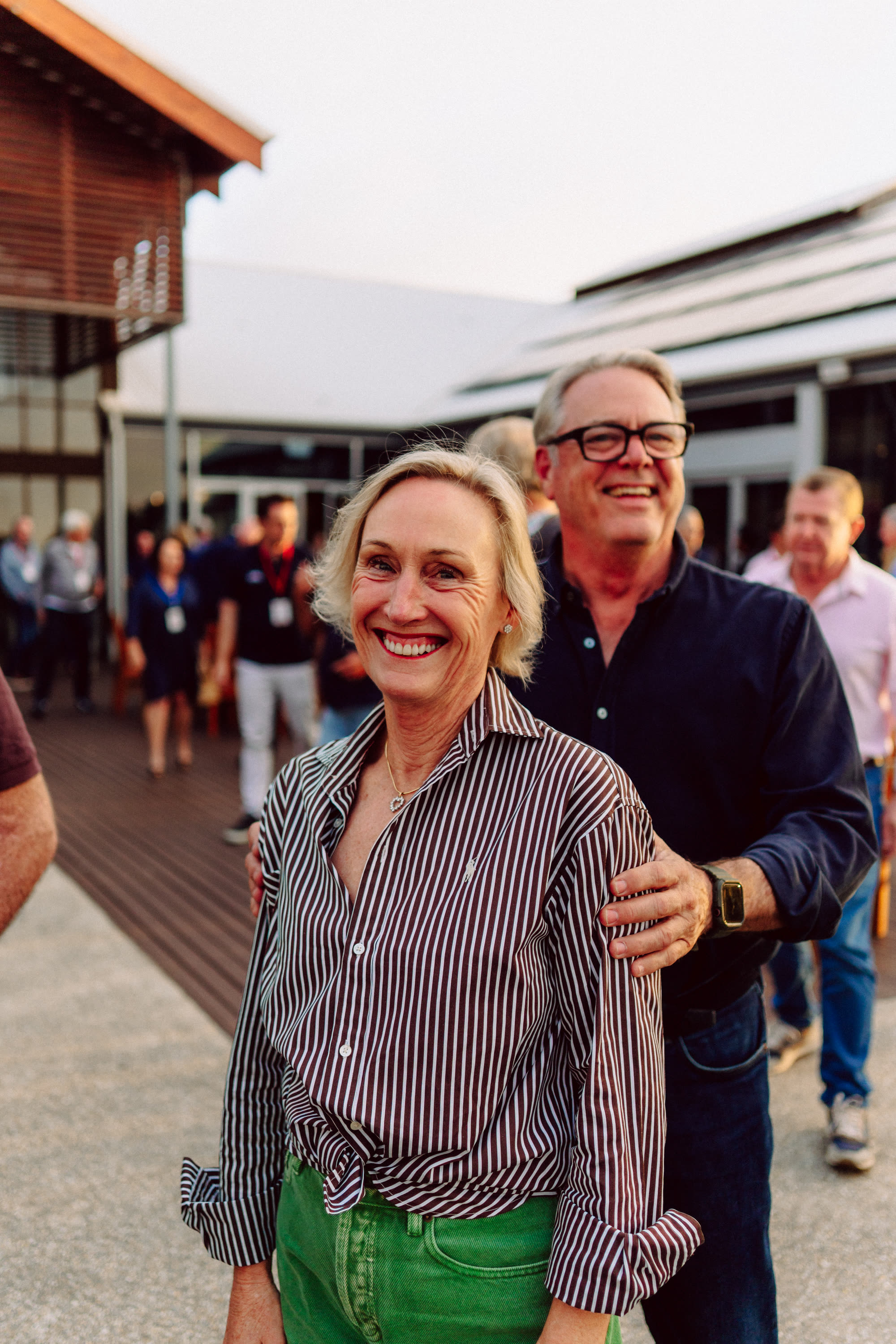 A woman and a man smiling among guests at an outdoor evening gathering