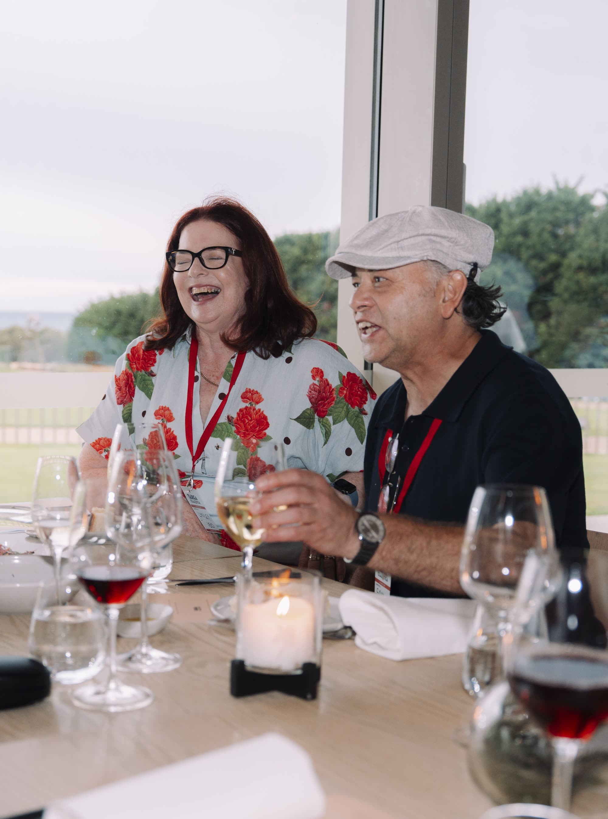 Two guests laughing at a dinner table set with wine glasses and a candle