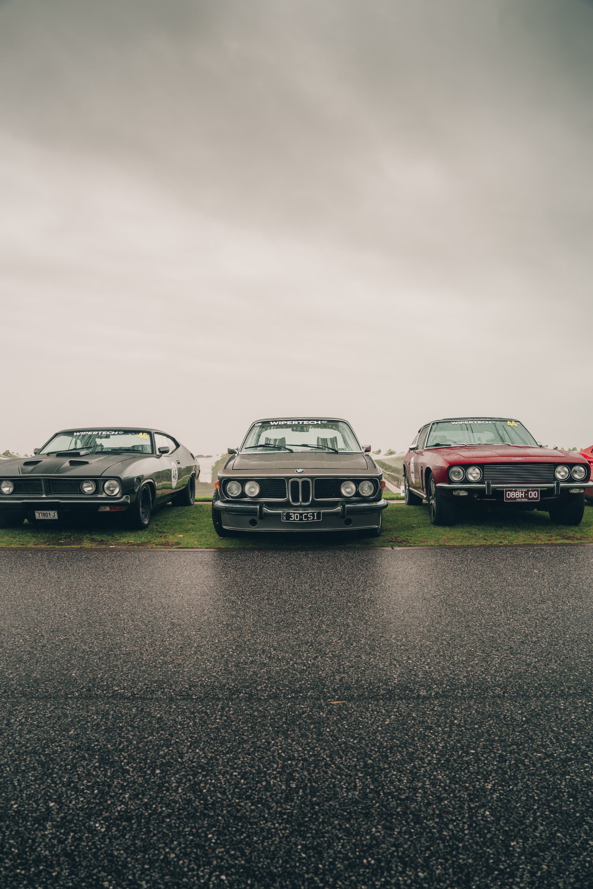 A black muscle coupe, a BMW coupe and a red coupe lined up on grass