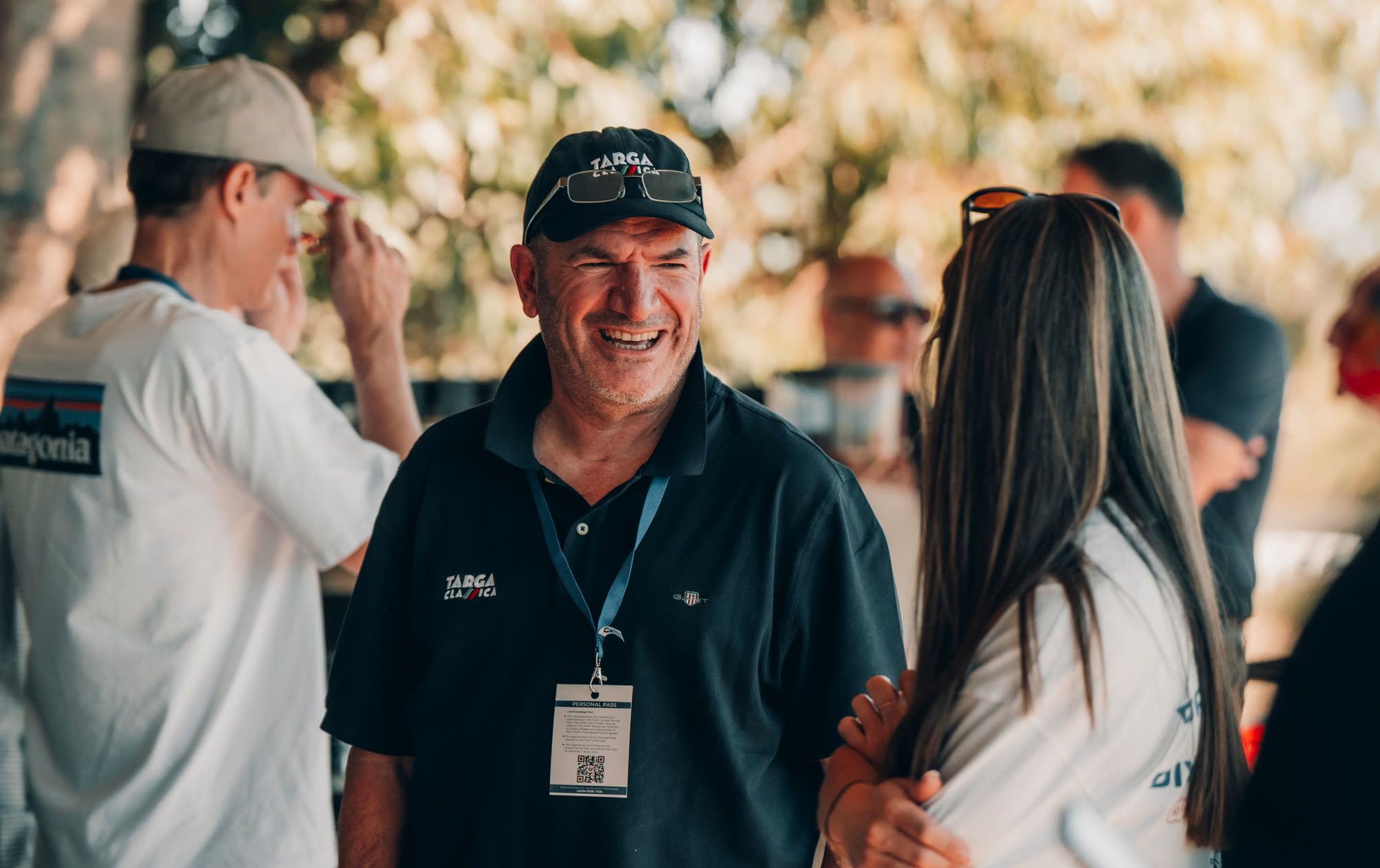 A man in a Targa Classica cap and polo laughing in conversation outdoors