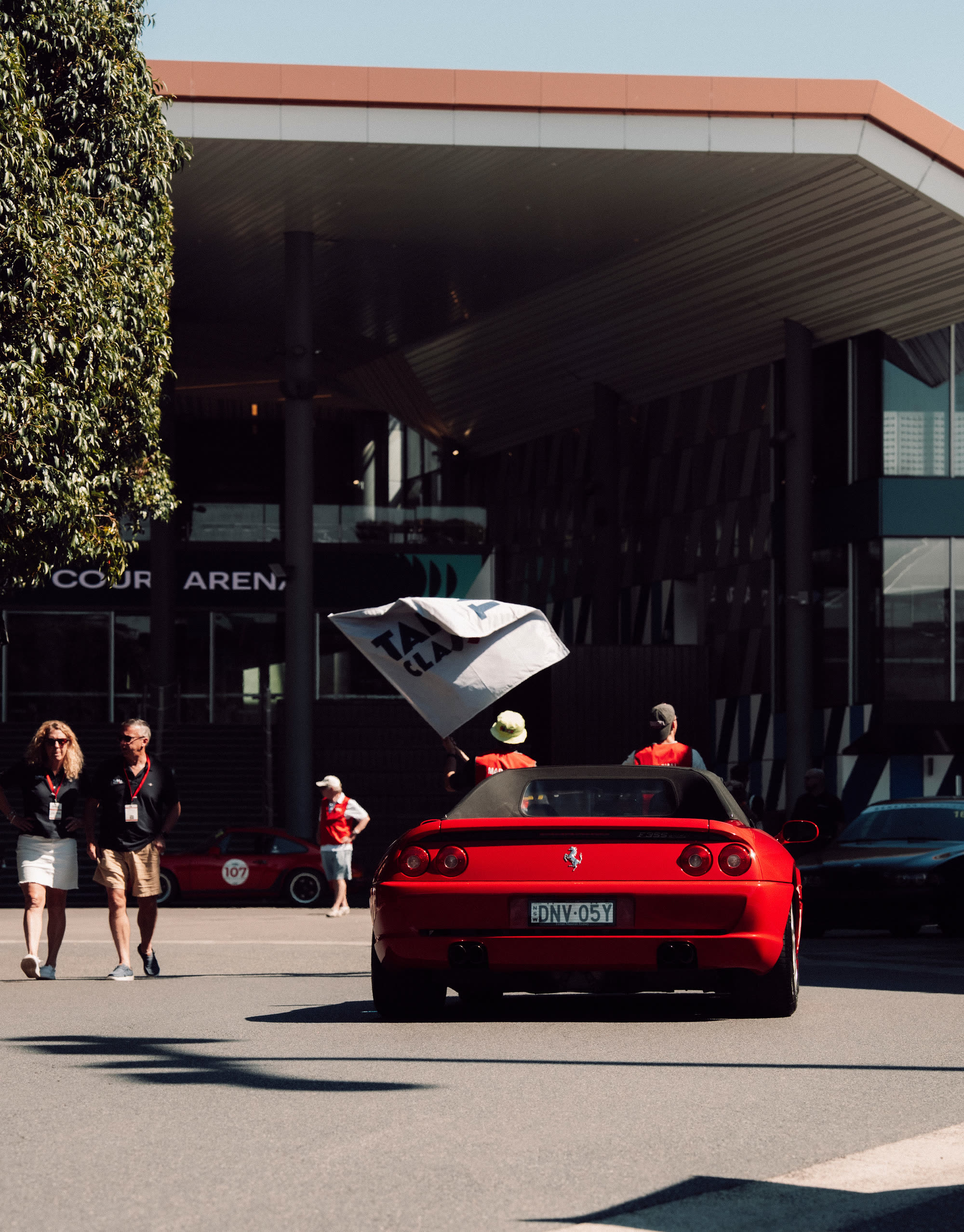 A red Ferrari convertible pulling away past spectators and an event flag
