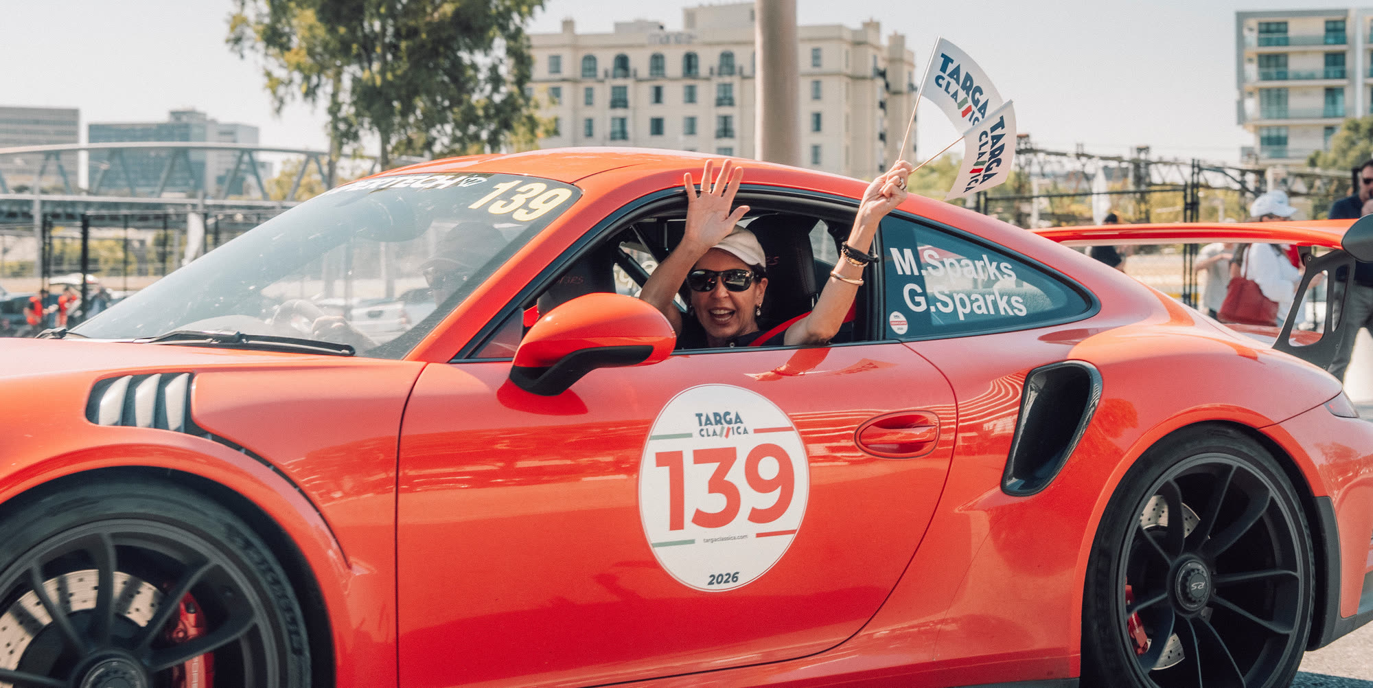 A co-driver waving a small flag from an orange Porsche 911 running number 139
