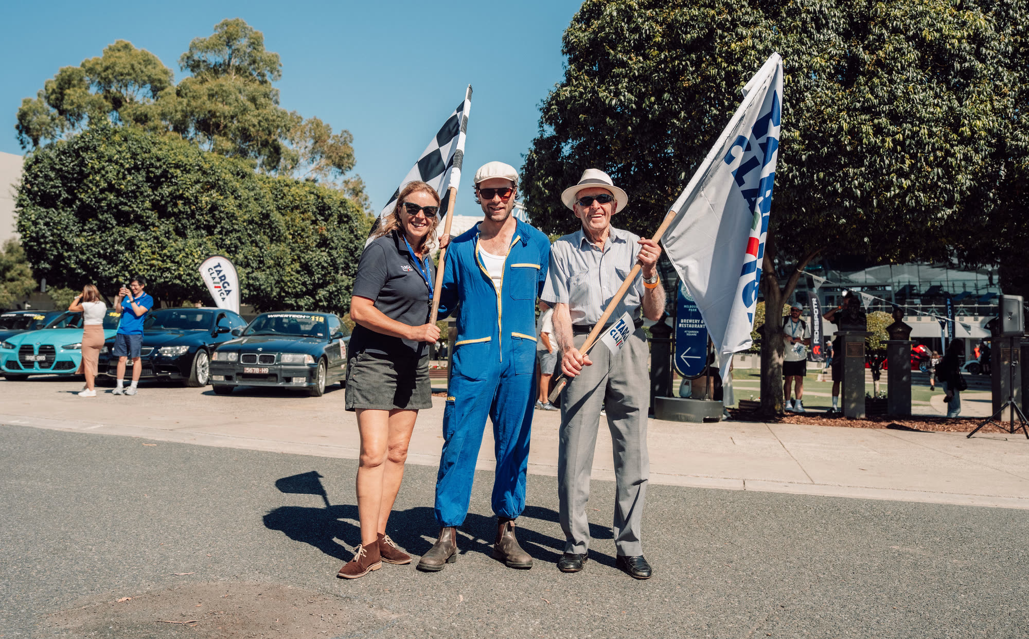 Three flag marshals posing with chequered and Targa Classica flags