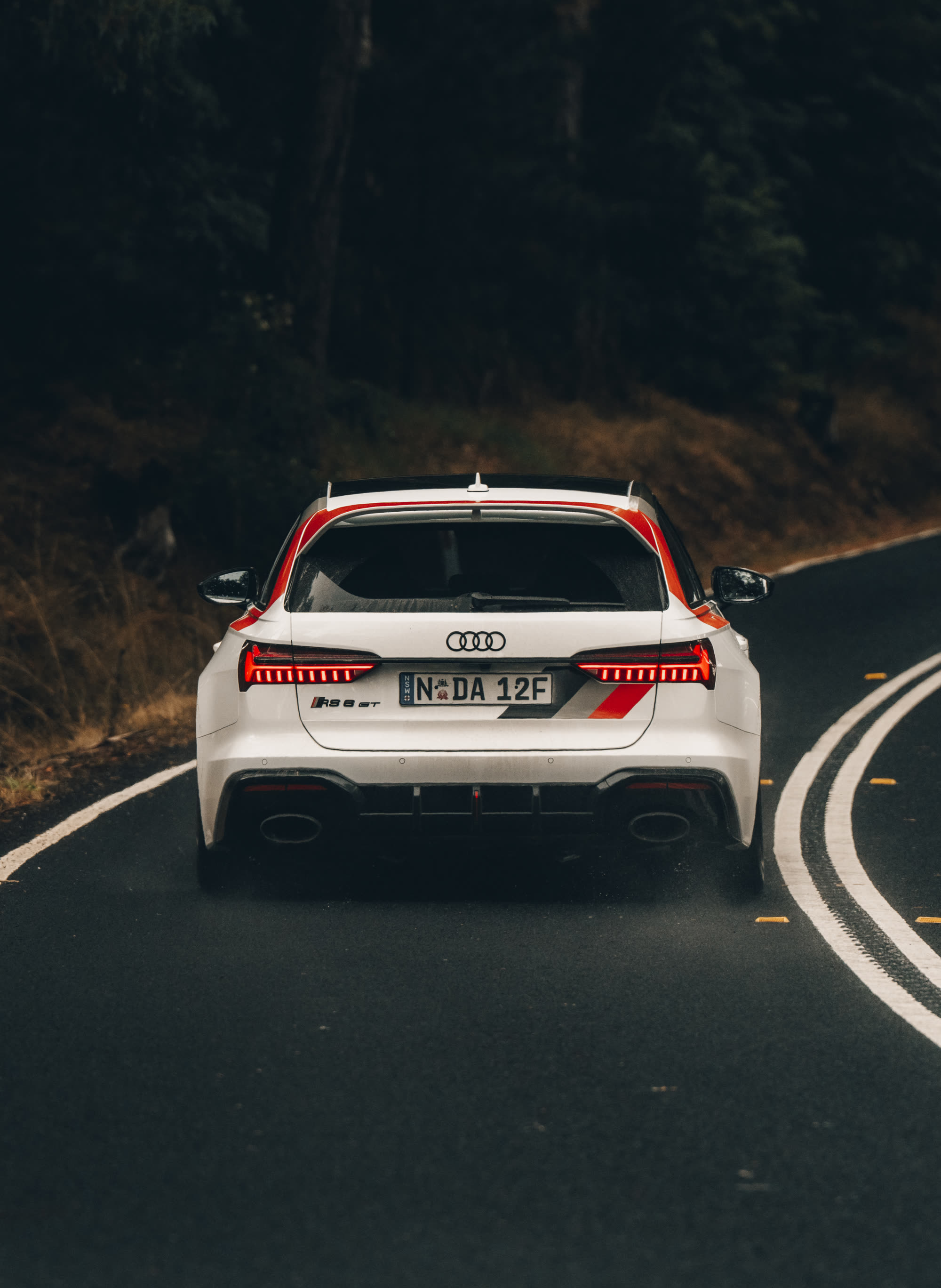 Rear of a white Audi RS6 wagon with red livery stripes on a forest road