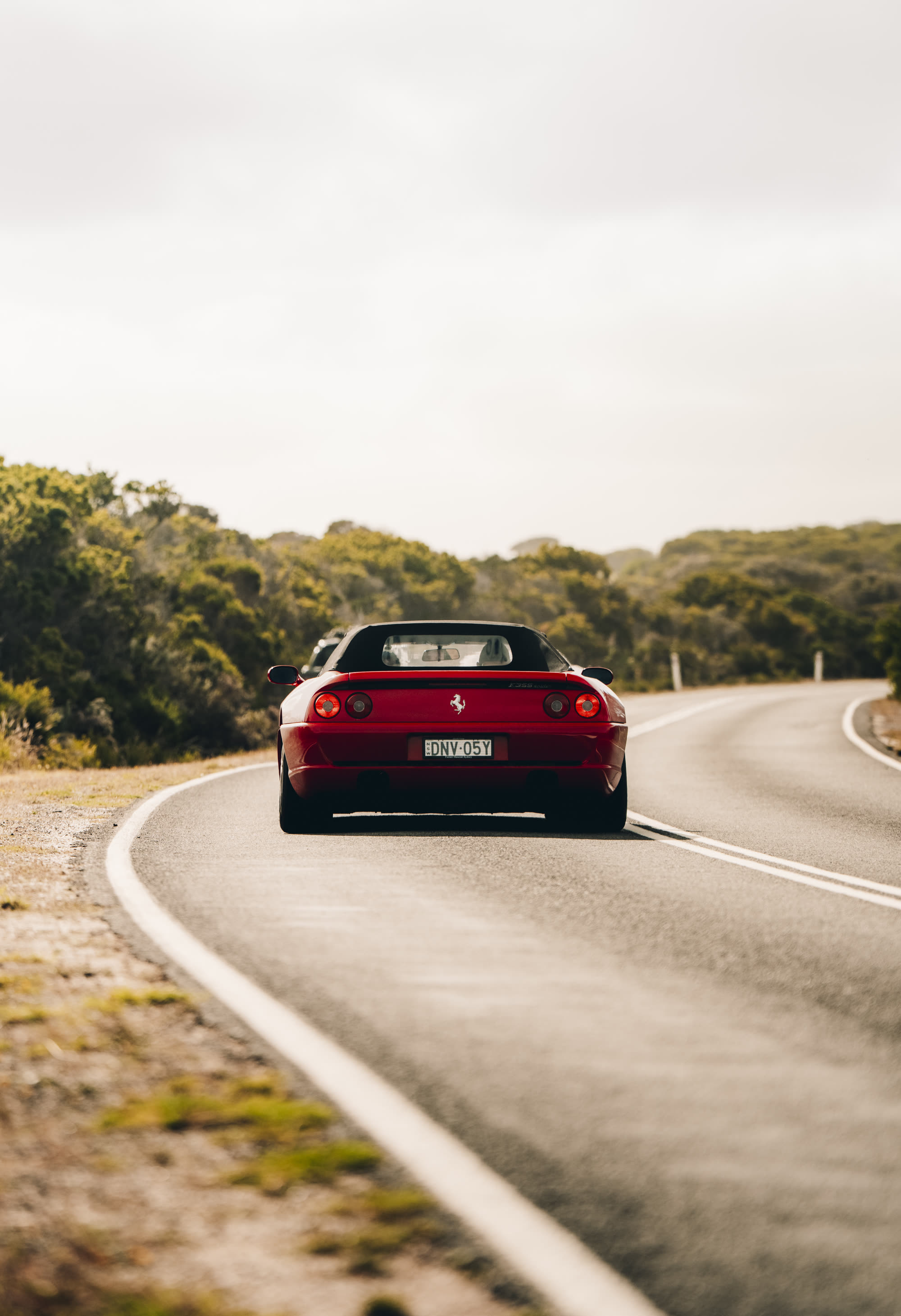 A red Ferrari convertible seen from behind on an open coastal road