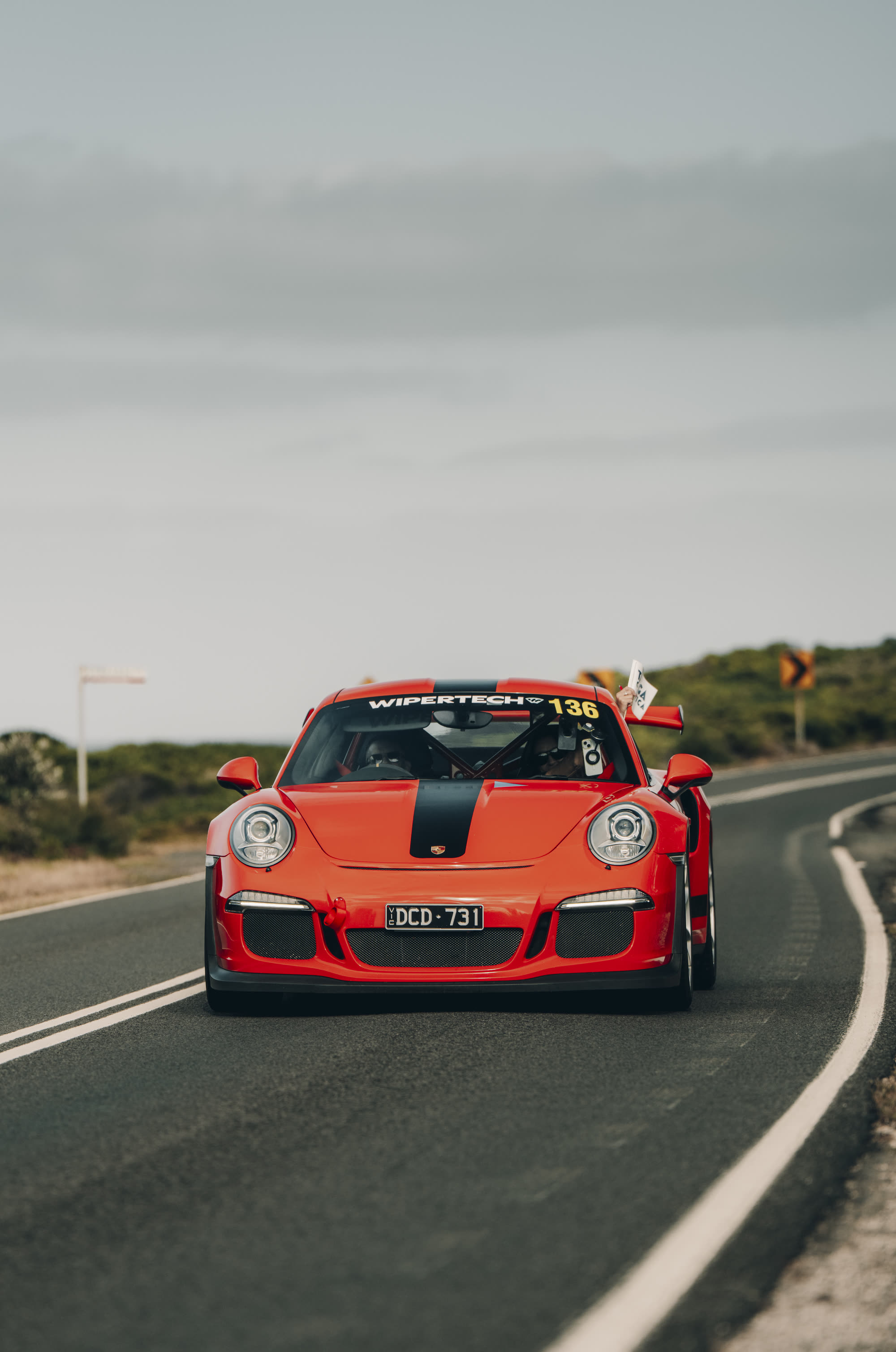 A red Porsche 911 GT3 head-on on a coast road, running number 136