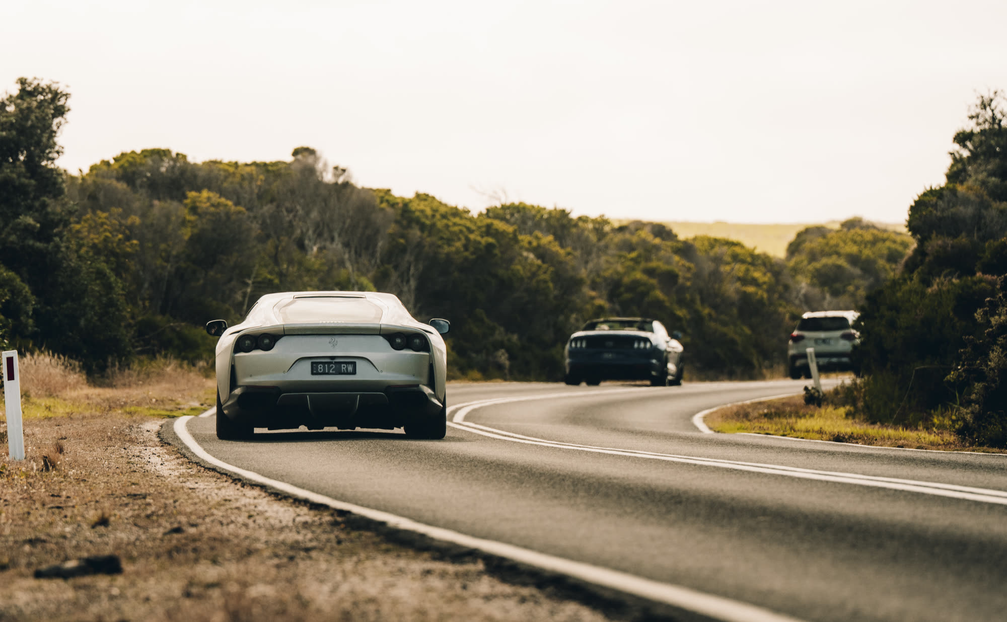 A silver modern grand tourer trailing other cars along a coastal highway
