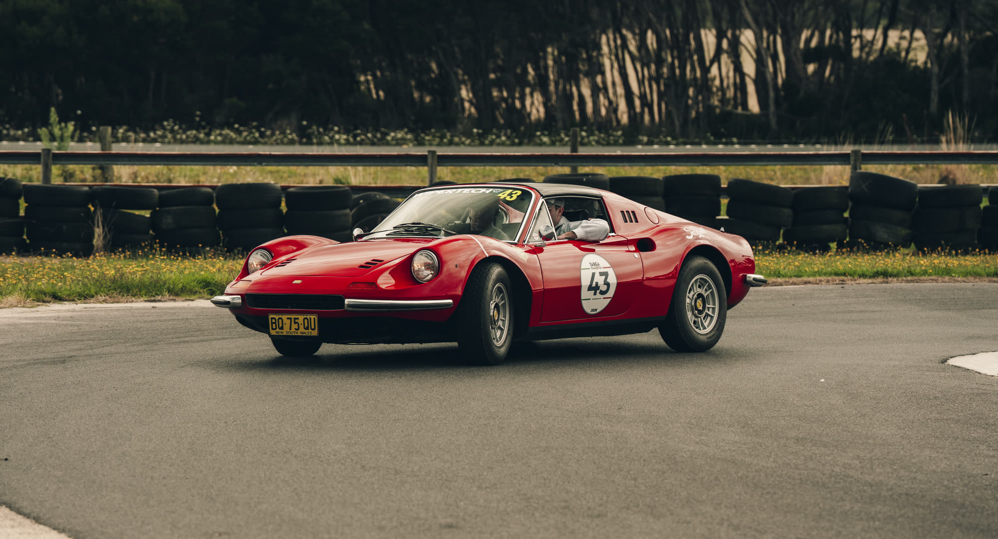 A red Ferrari Dino on a closed circuit lined with tyre barriers