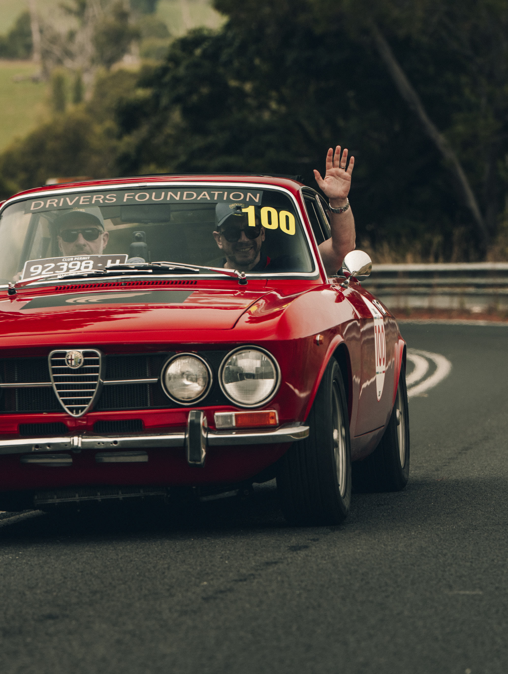 A red Alfa Romeo coupe with its passenger waving, running number 100