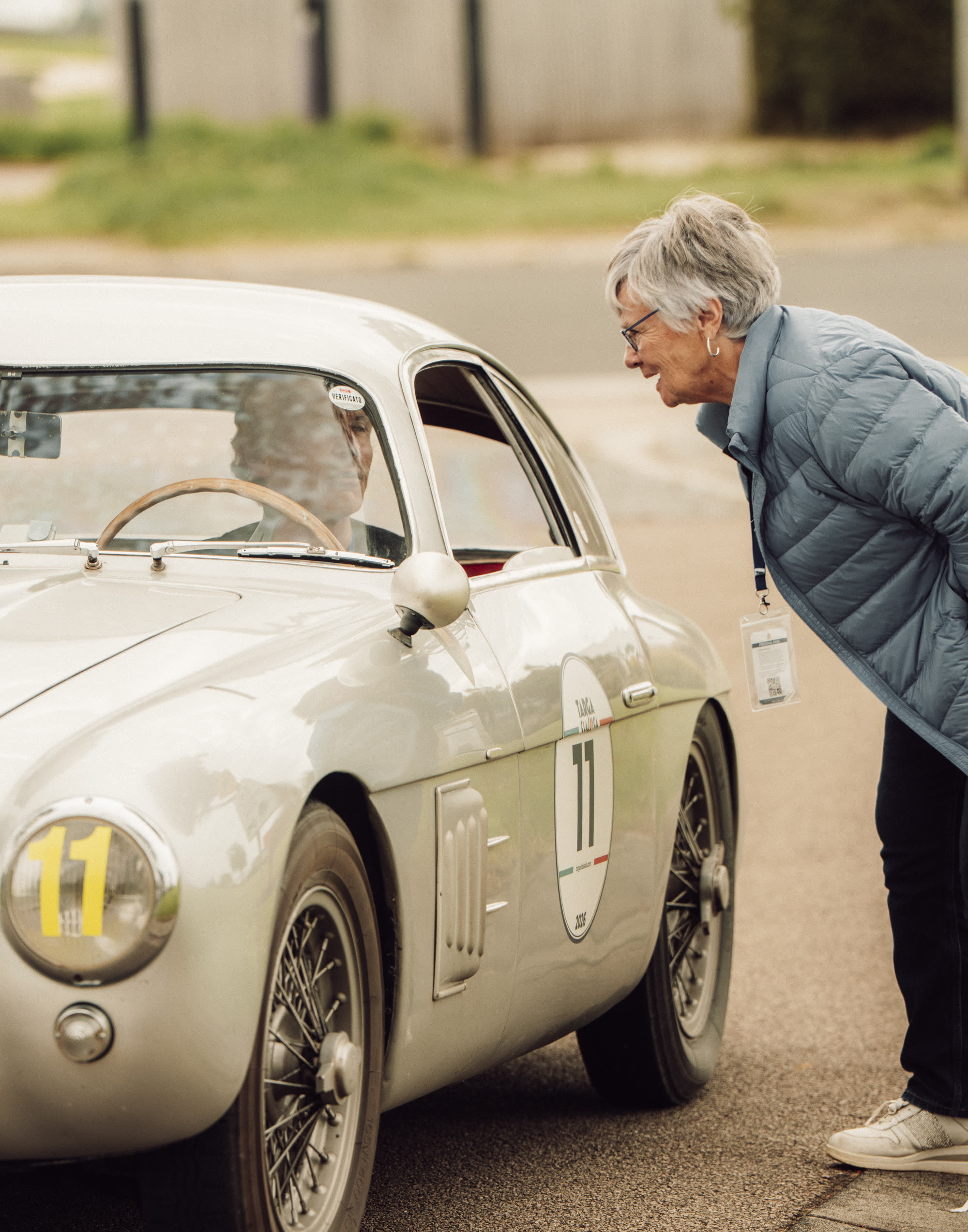 A woman leaning in to talk to the driver of a silver 1950s coupe