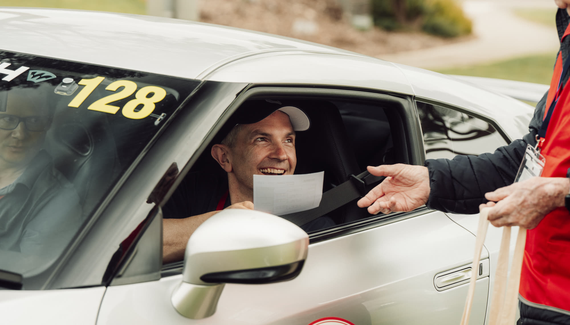 A driver taking a time card from a marshal through the window of a white car