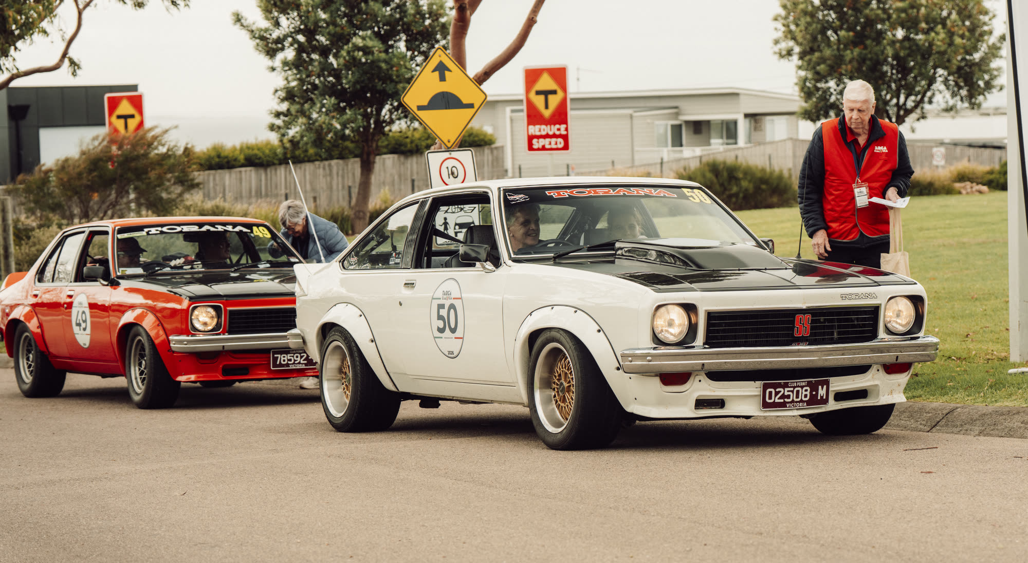 Two Holden Torana hatchbacks waiting at a checkpoint on a suburban street