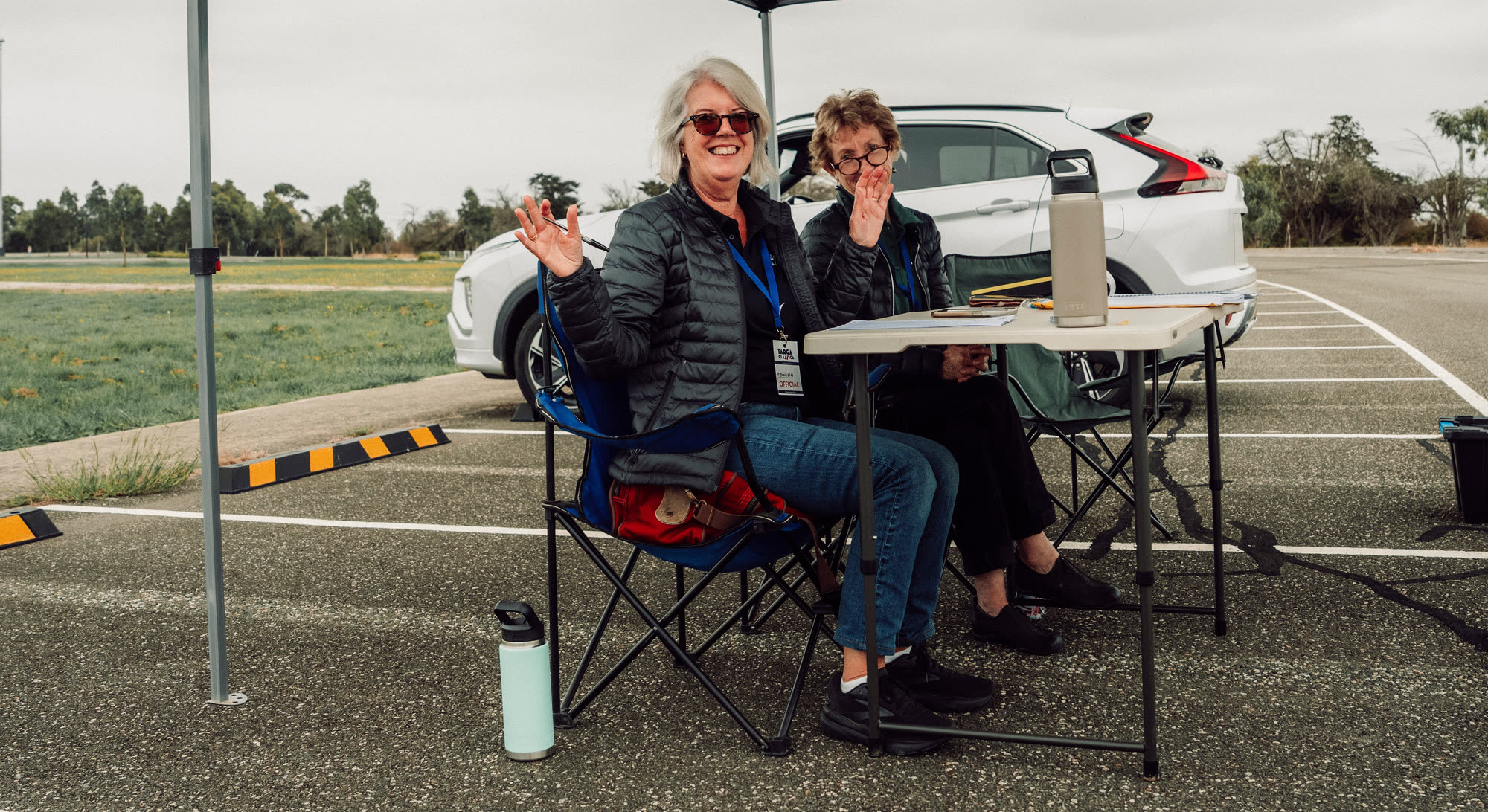 Two volunteers waving from the timing table under a gazebo