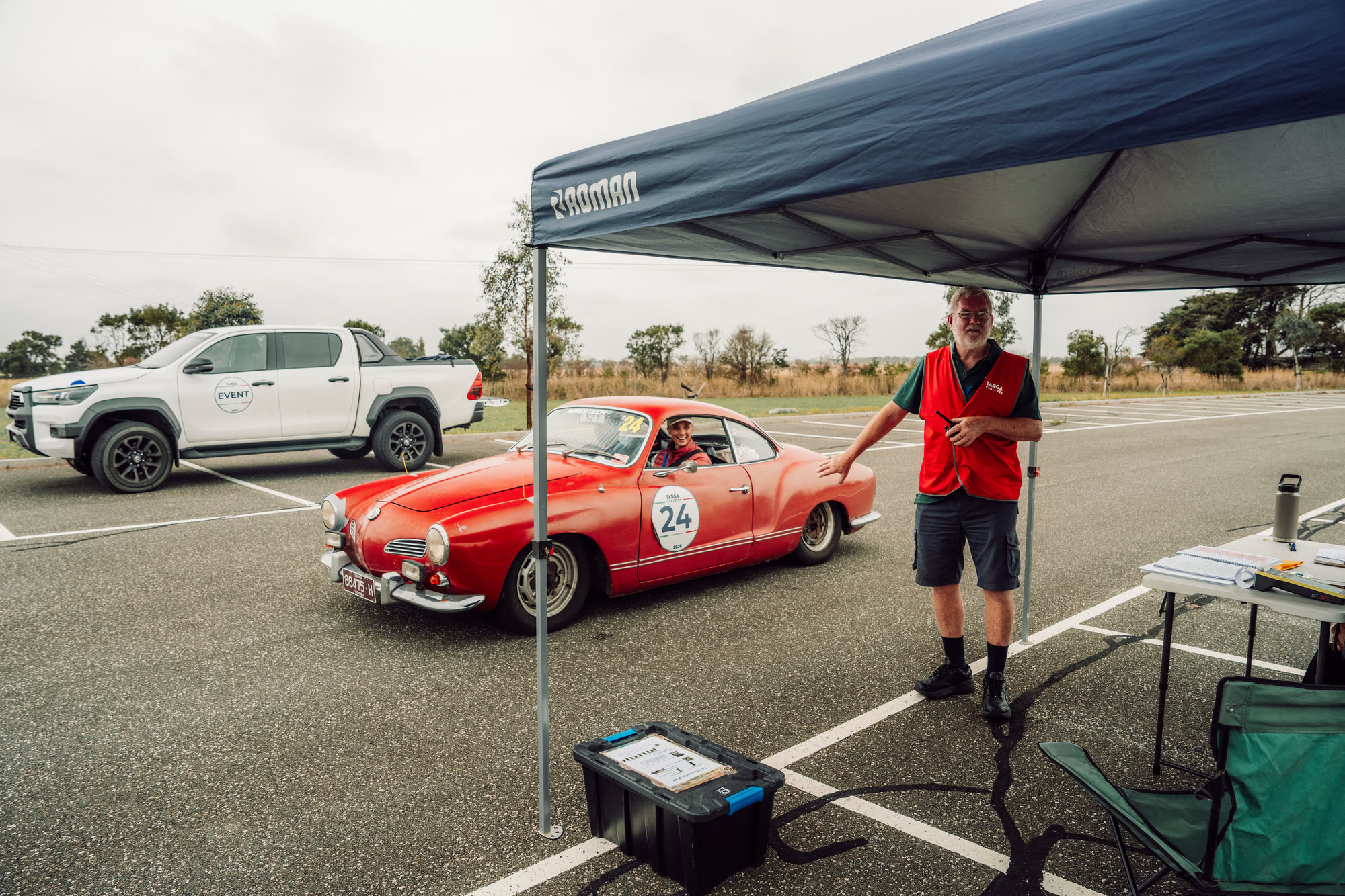 A red Karmann Ghia pausing at a marshal's gazebo in an open car park