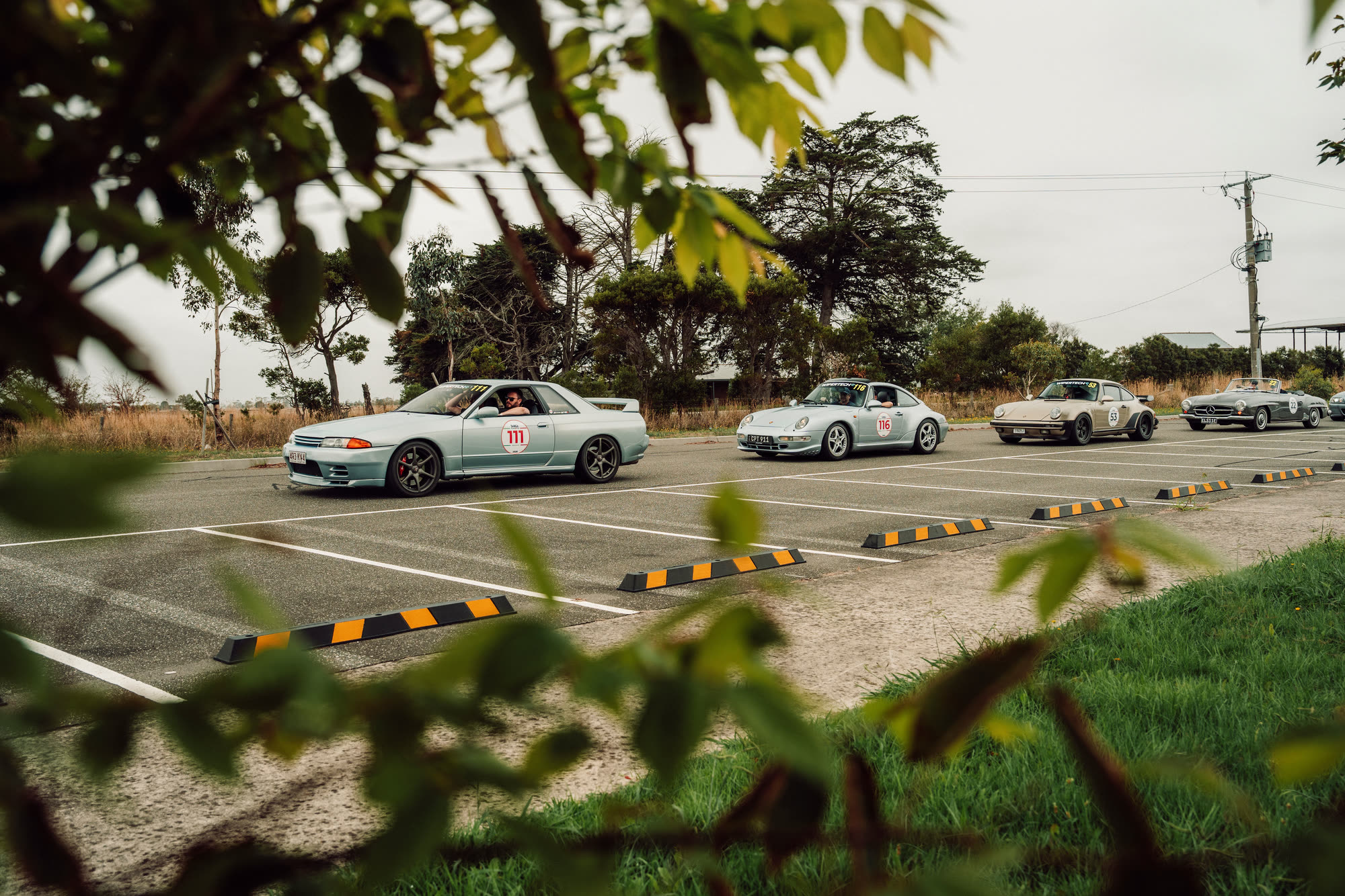 Cars queued in a rural car park, including two Porsche 911s and a Mercedes
