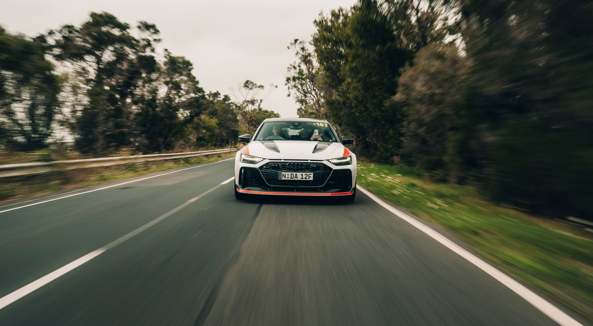 A white Audi RS6 tracked head-on along a country road at speed