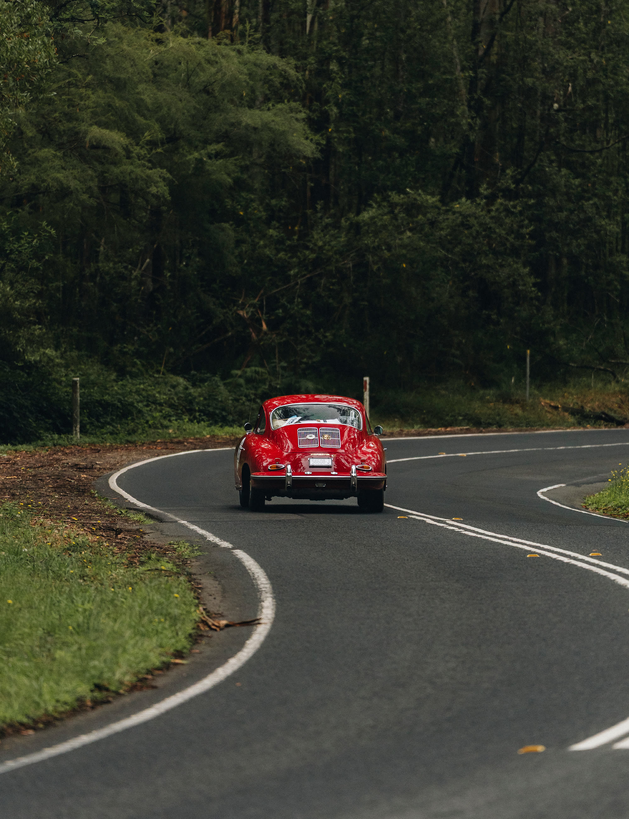 A red Porsche 356 coupe seen from behind on a wet forest road