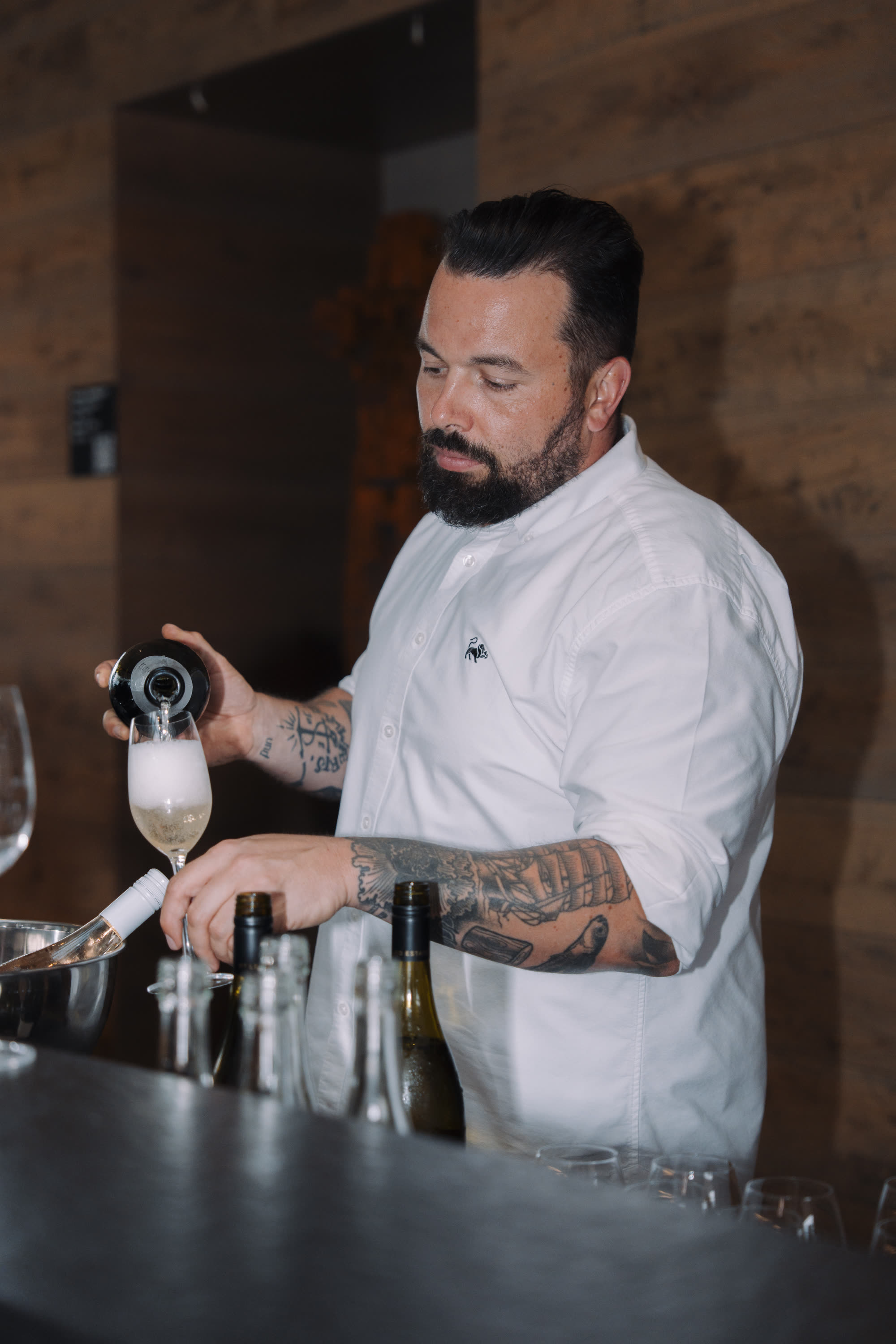 A man in a white shirt pouring sparkling wine behind a bar