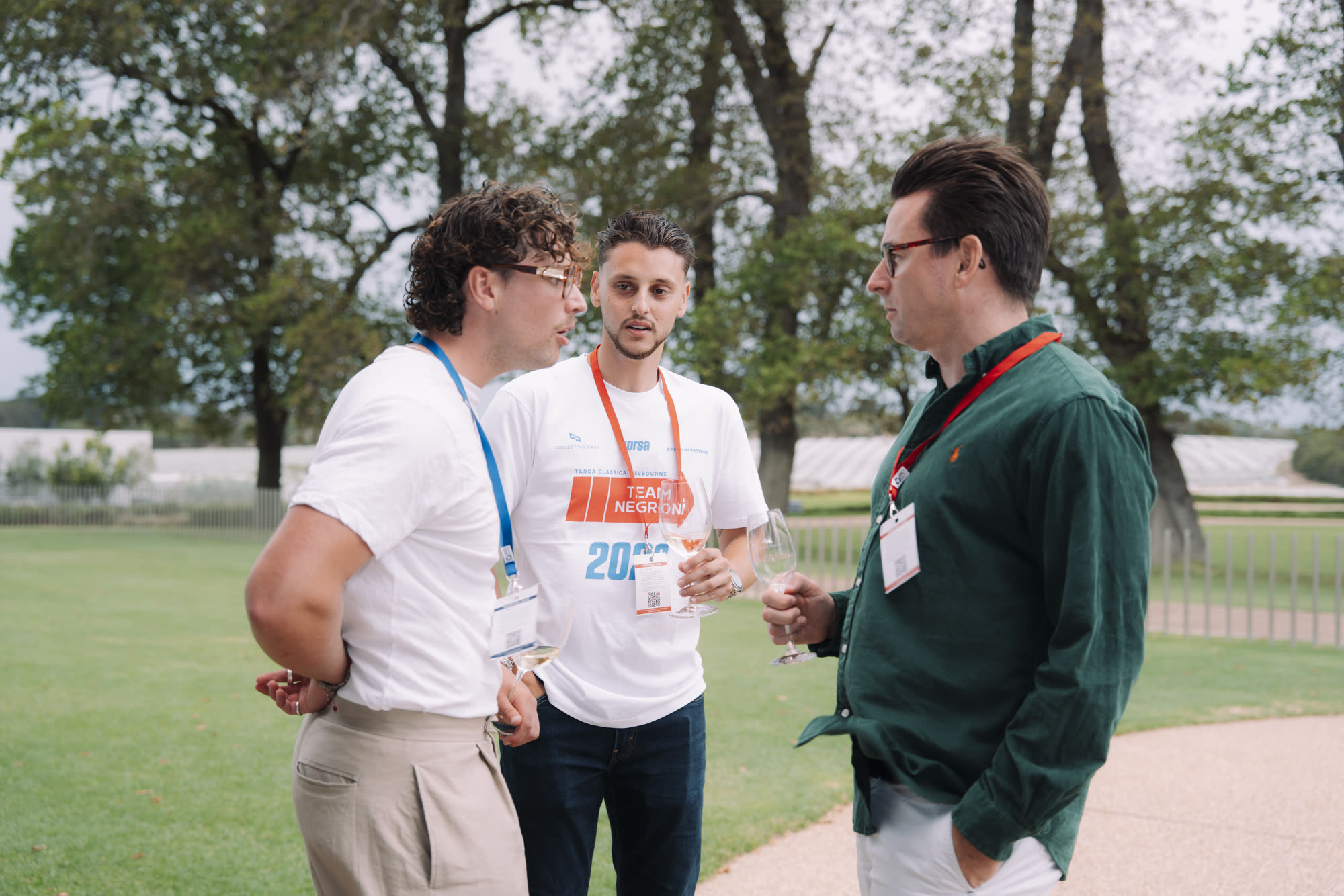 Three men talking with wine glasses in hand on a lawn
